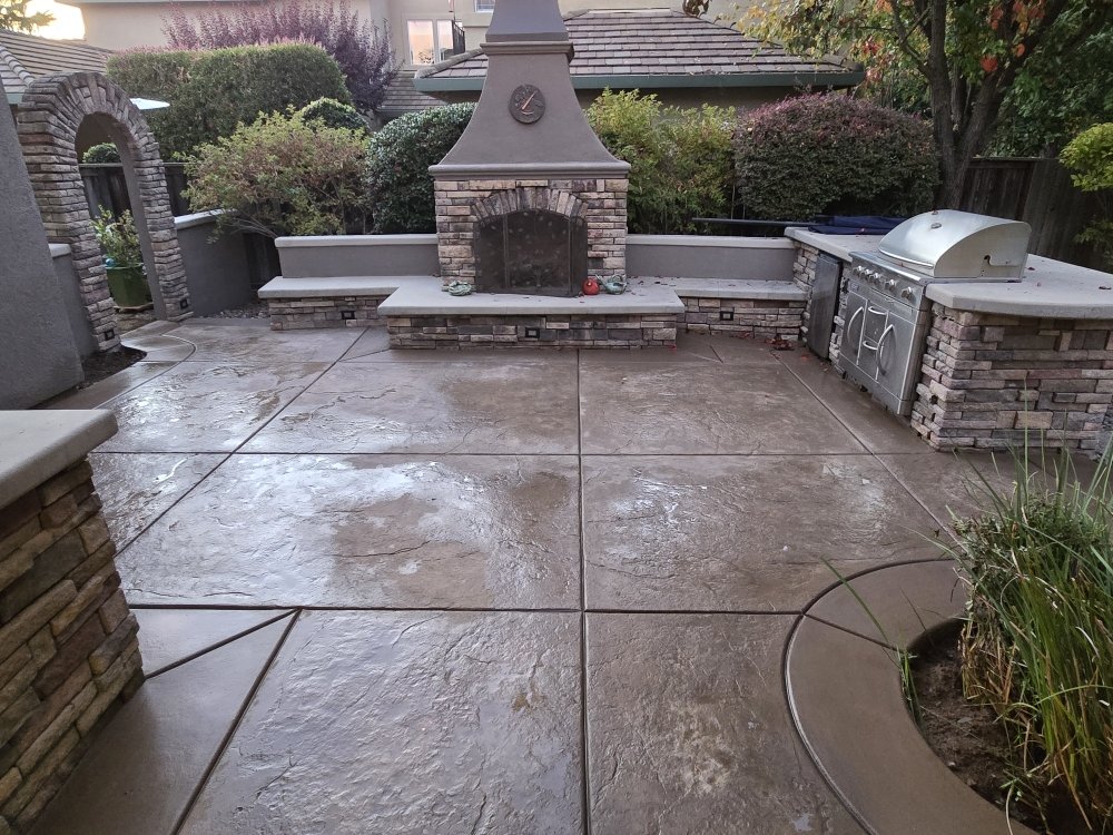 Stamped concrete patio featuring outdoor fireplace, built-in seating, and BBQ area with stone veneer accents