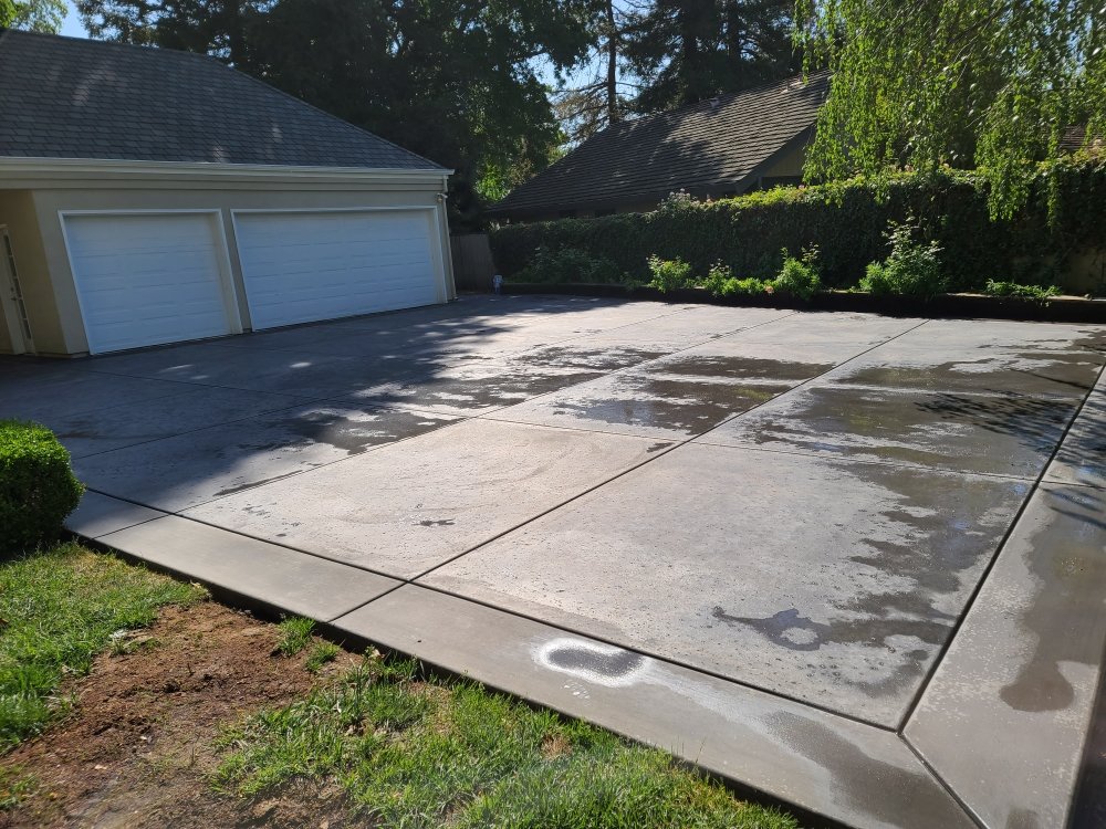Newly poured concrete driveway with expansion joints extending from two-car garage in residential backyard setting