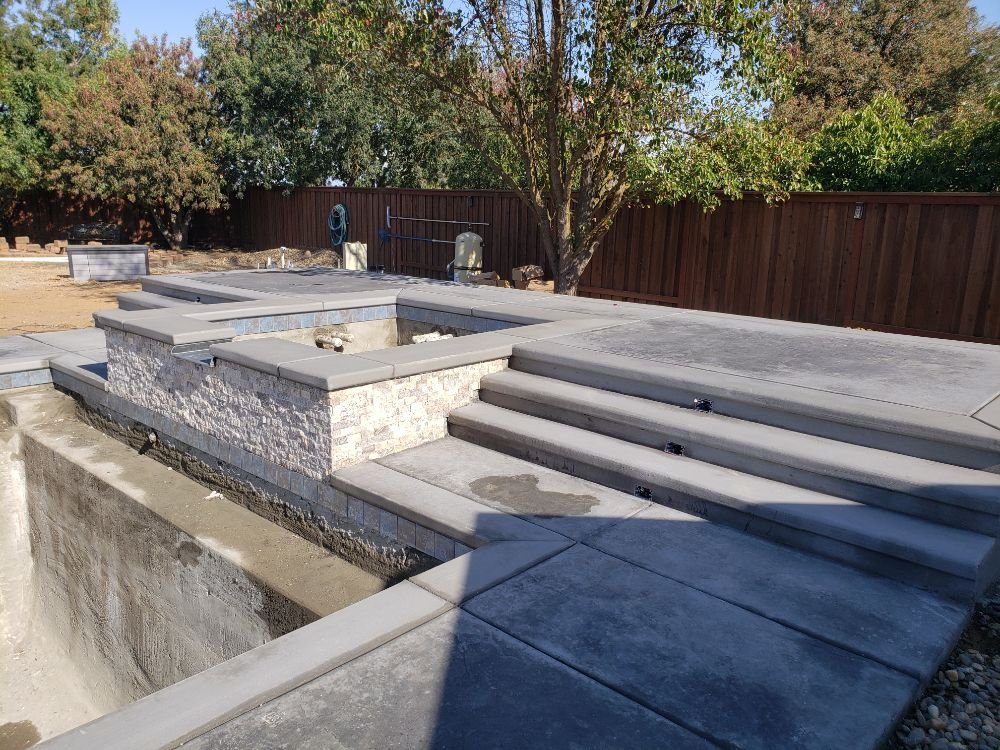 Multi-level concrete pool deck with stone veneer walls and integrated steps in residential backyard