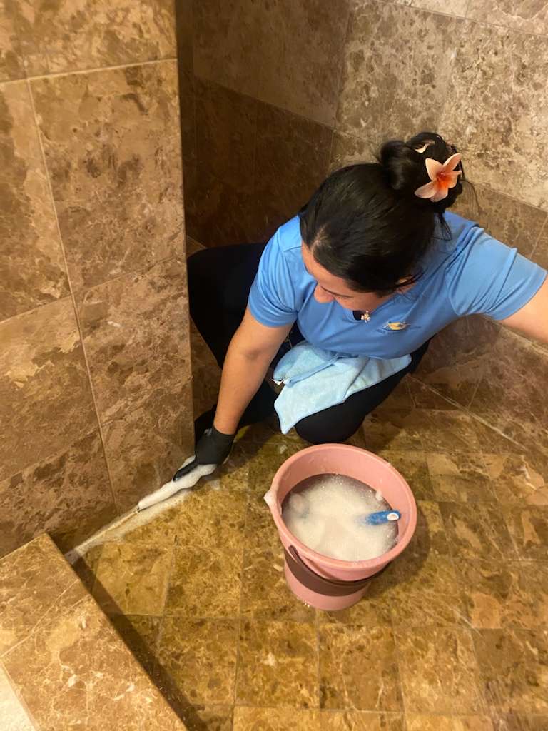 Professional cleaner scrubbing marble tile floor and walls during deep cleaning service in Elk Grove bathroom