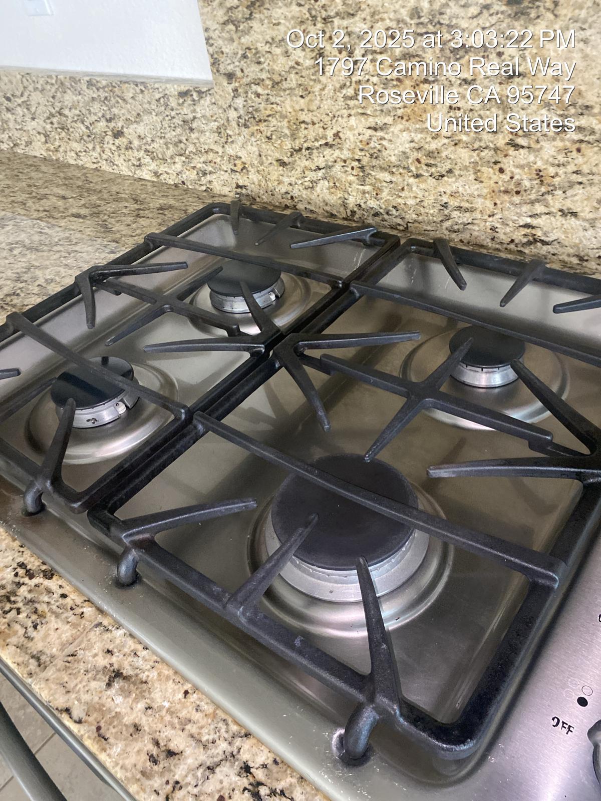 Sparkling clean gas stovetop with black grates and burners against granite countertop and backsplash